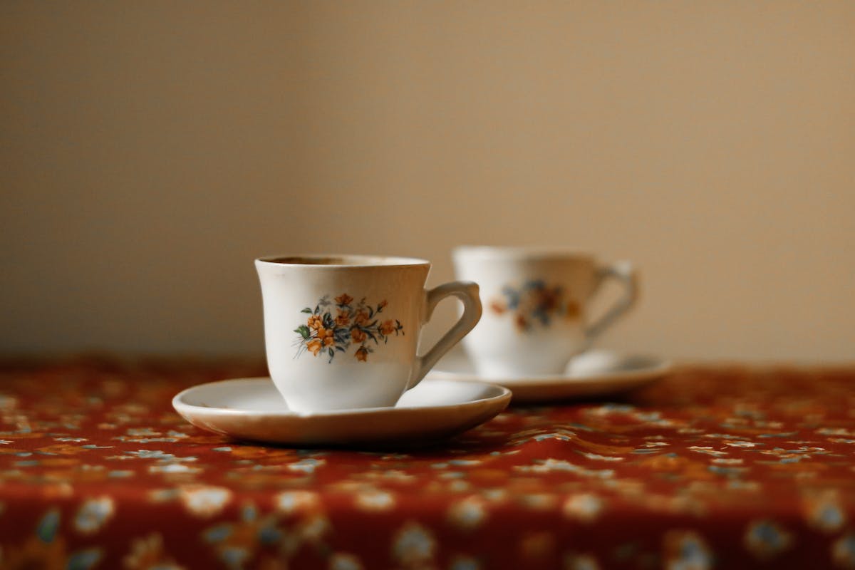 Two porcelain mugs on a red floral tablecloth — Cluj, October 2023
